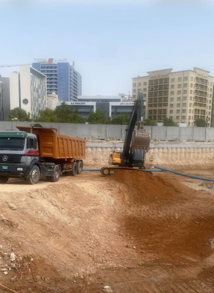 Excavator and dump truck moving earth for site backfilling beside urban buildings