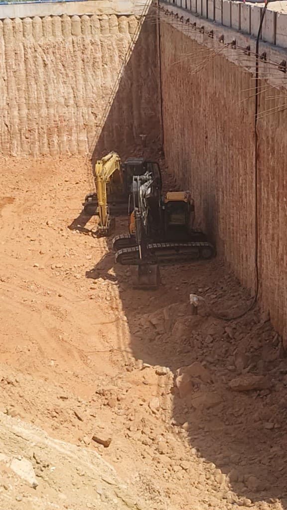 Looking down into a shored excavation pit with two excavators on the floor