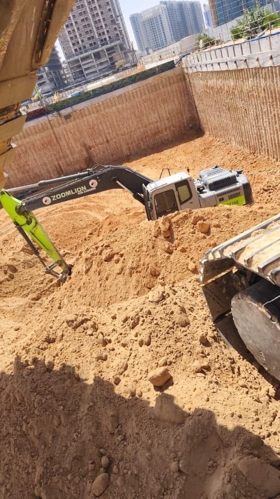 Excavator digging beside piled shoring walls on a city construction site